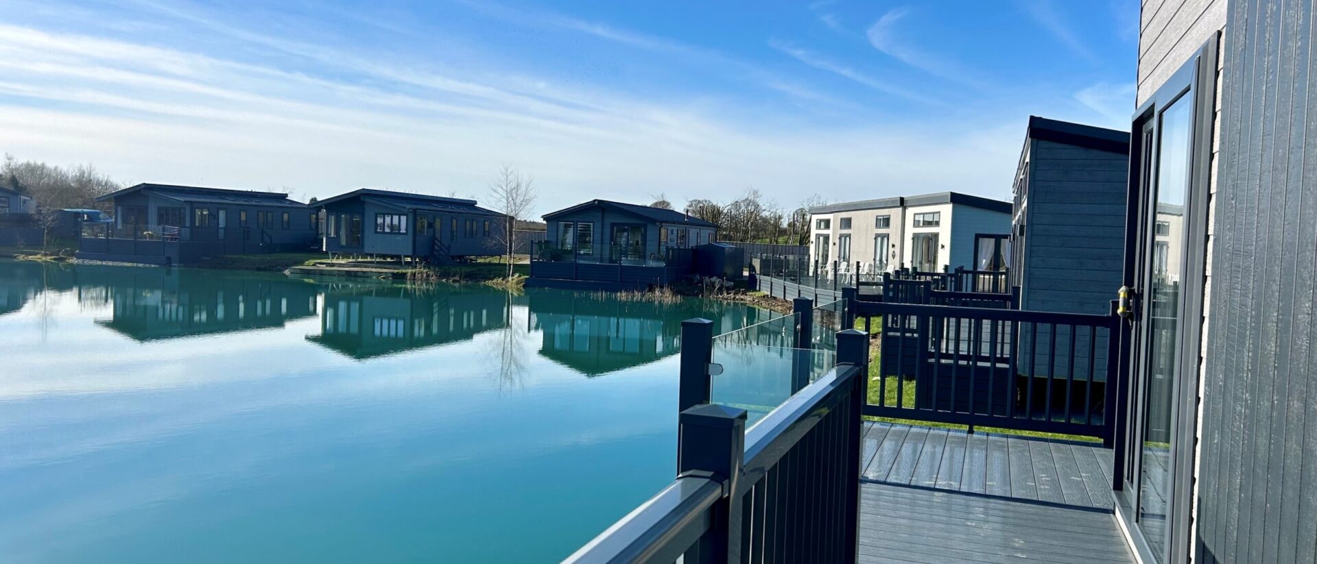 Wide view across the turquoise fishing lake at Derwent Oaks, with lakeside lodges and private decking beyond